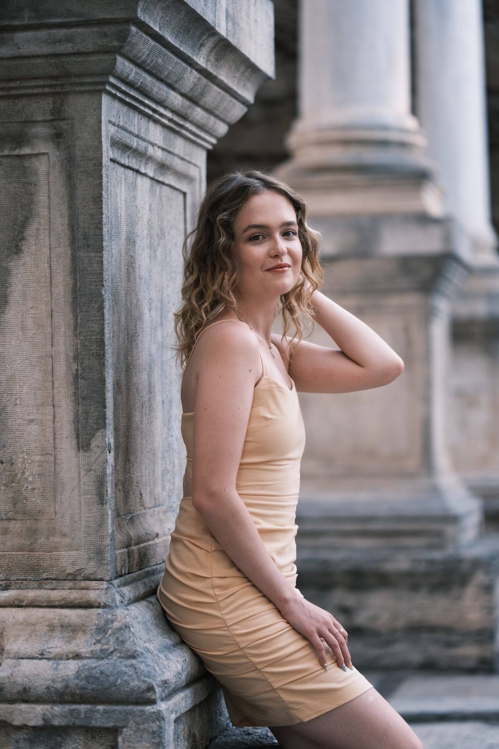 Woman in a beige dress leaning on carved stone at Hadrian's Gate