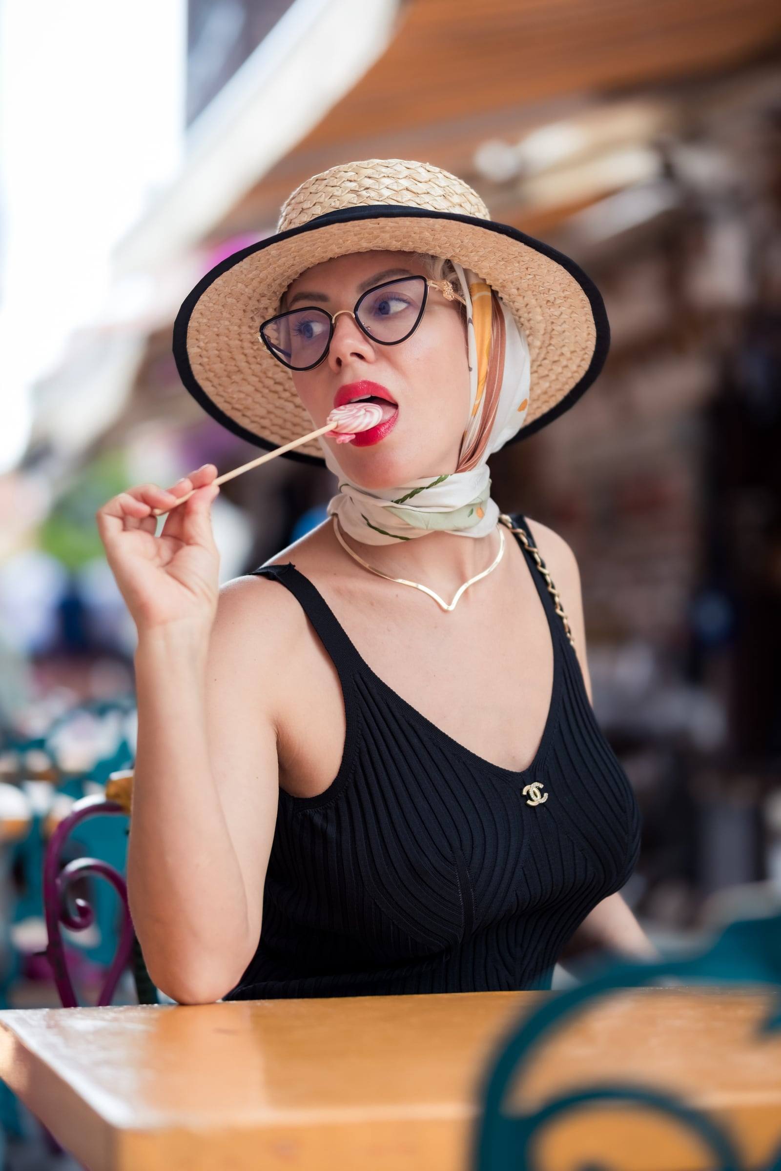Woman in a straw hat with a lollipop at a café table