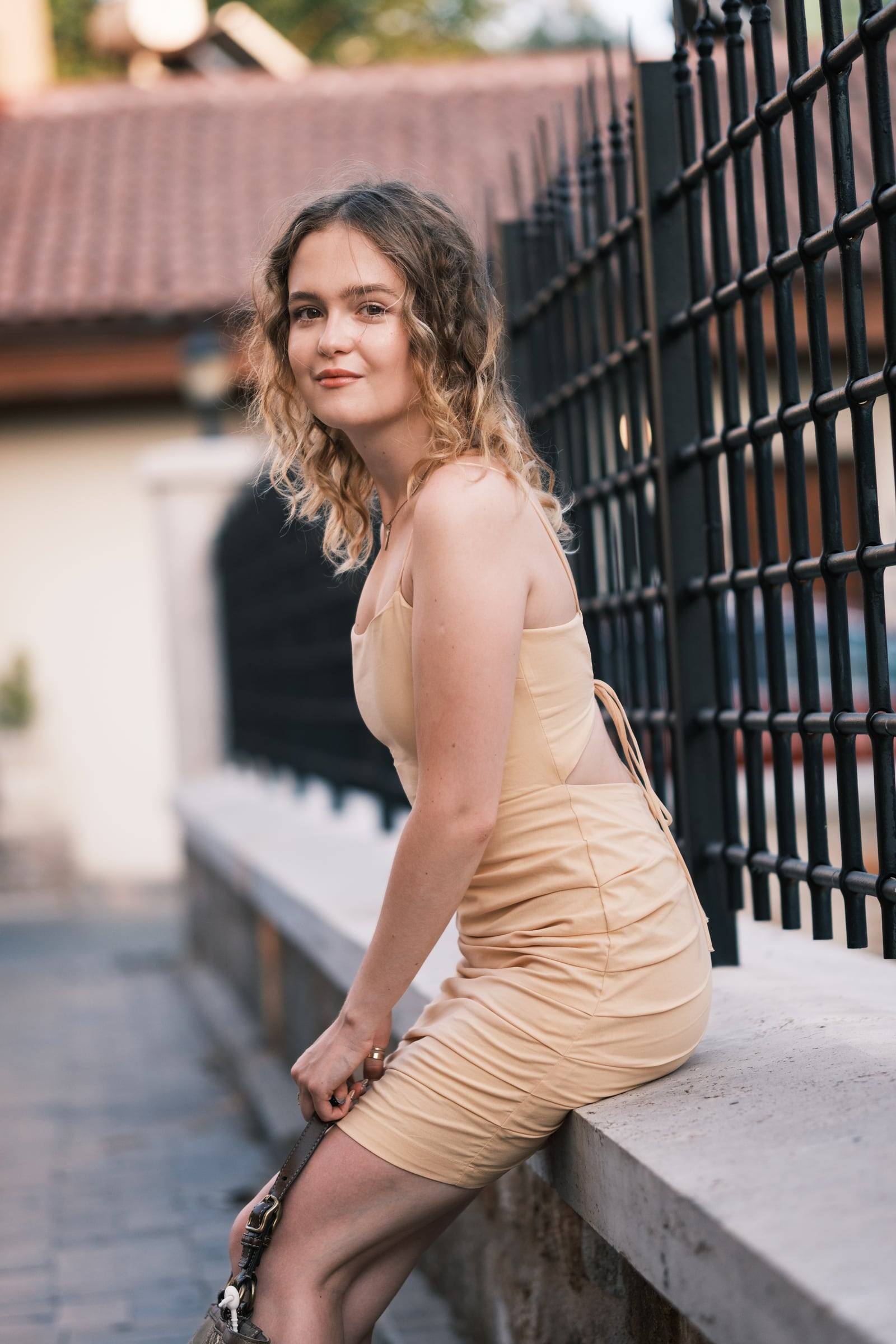 Woman in a beige dress sitting by an iron railing in Kaleiçi