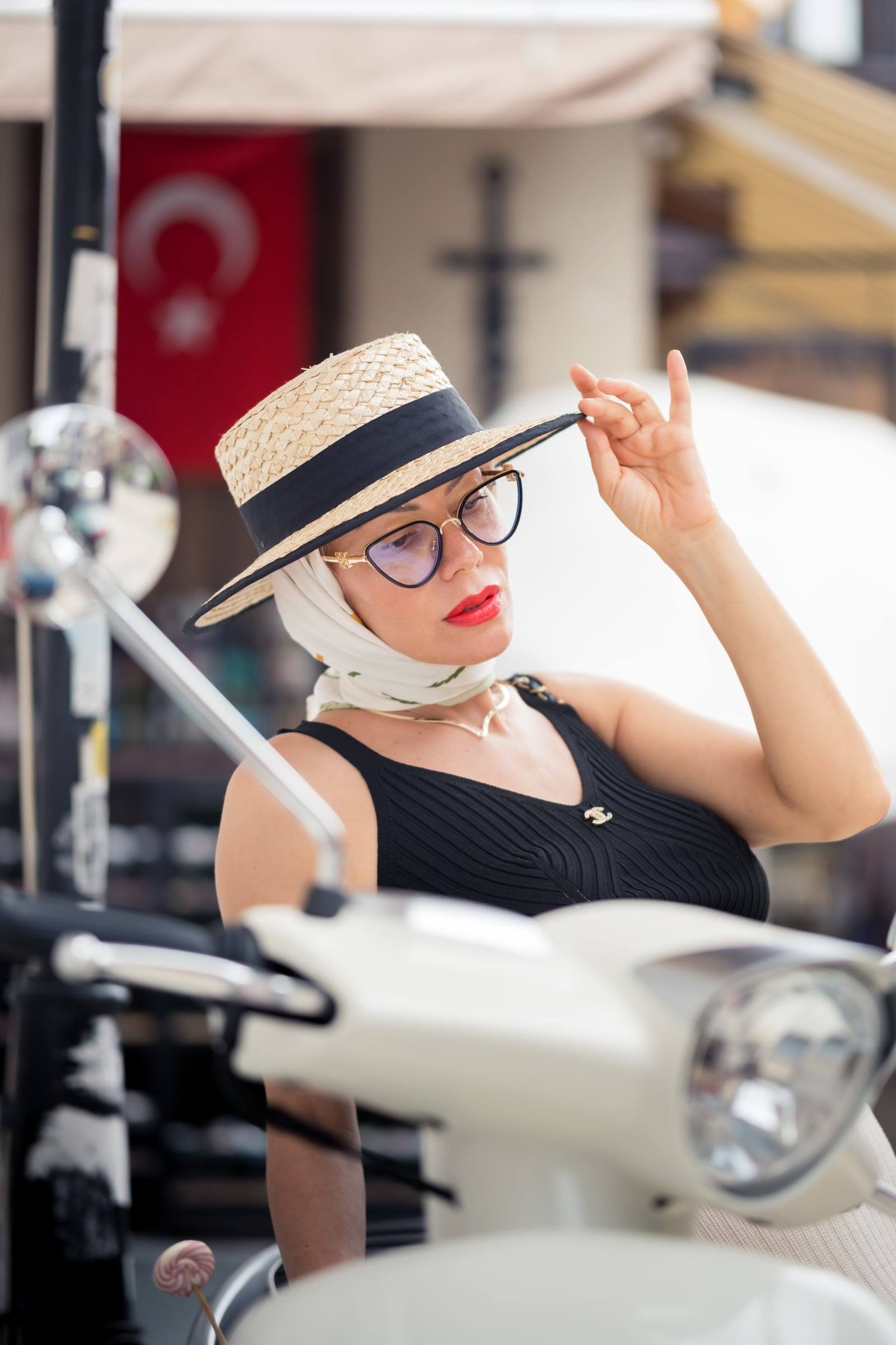 Woman in a boater hat on a vintage scooter with a Turkish flag behind