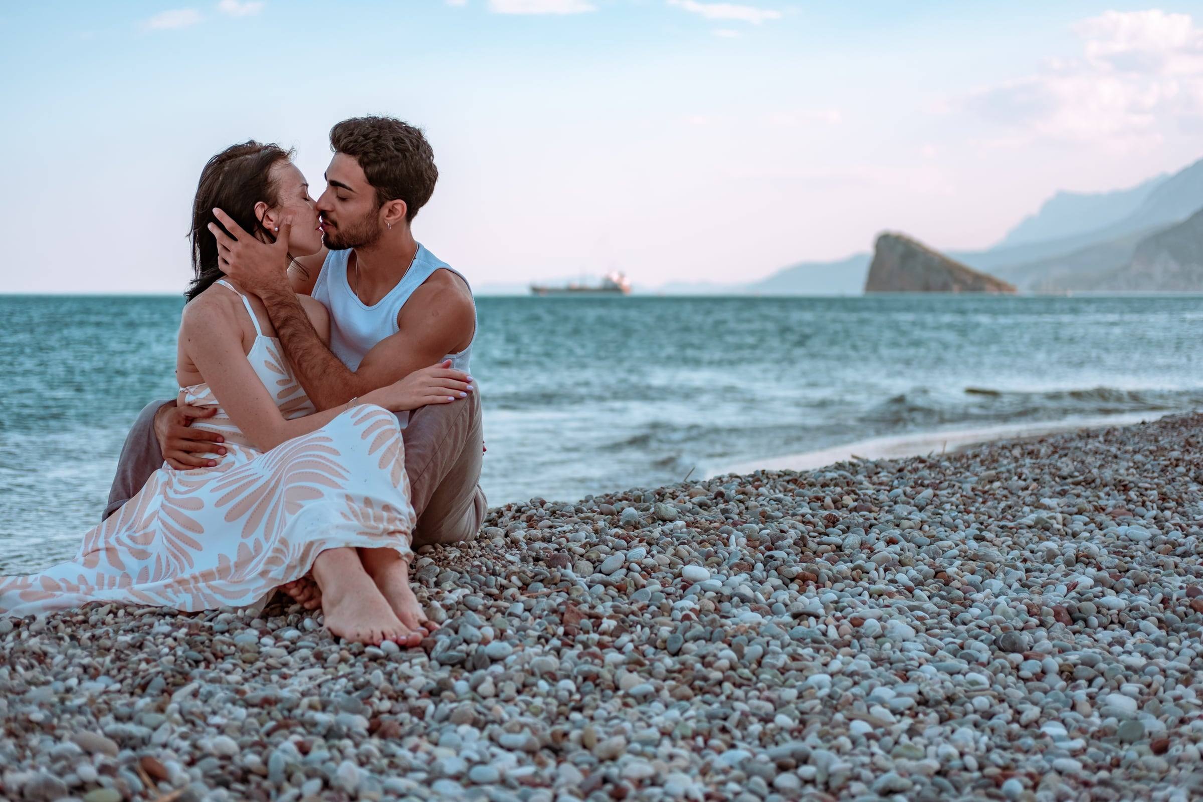 Couple sitting on a pebble beach with a rock island behind