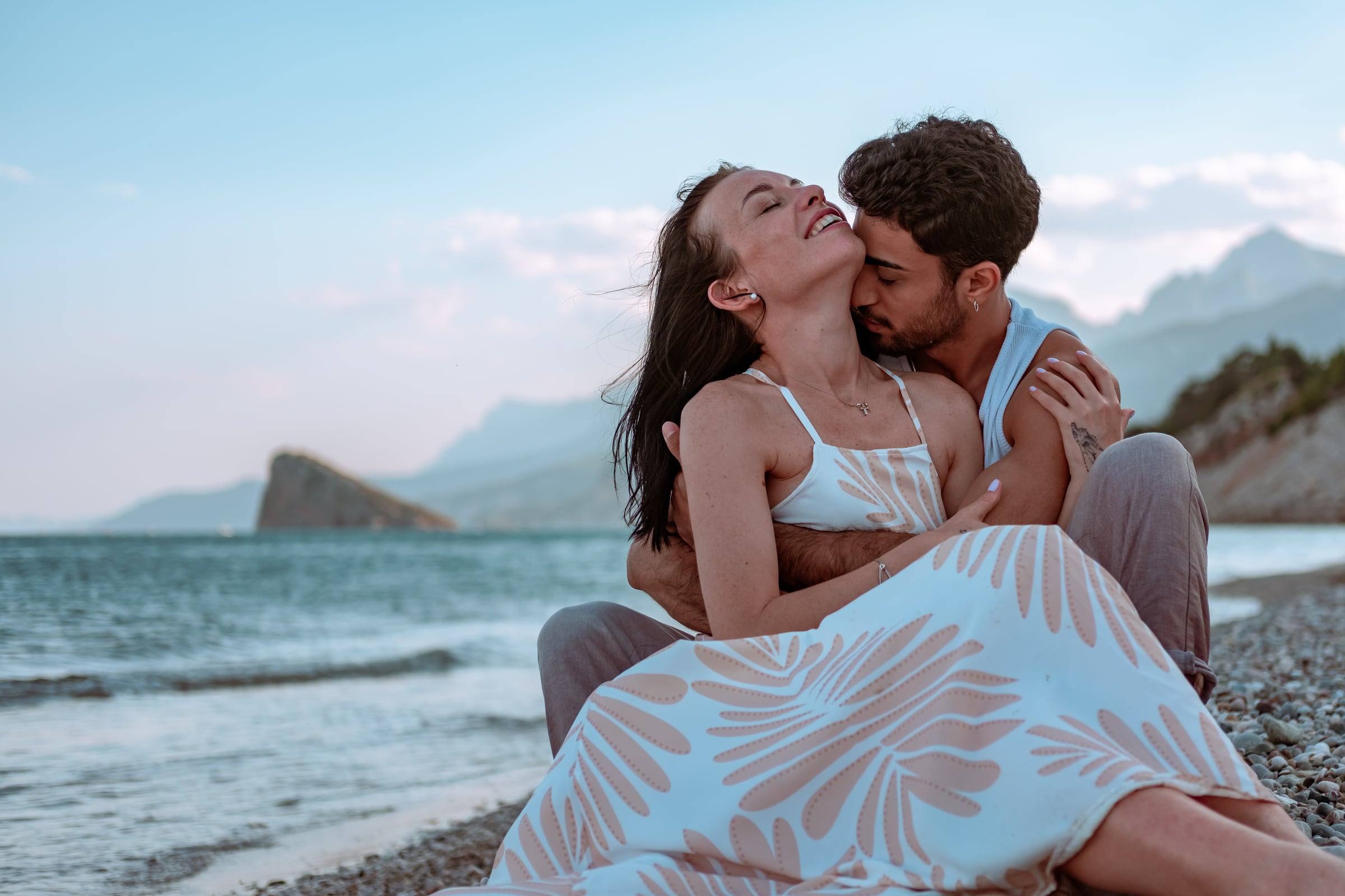Laughing couple embracing on the beach with mountains behind