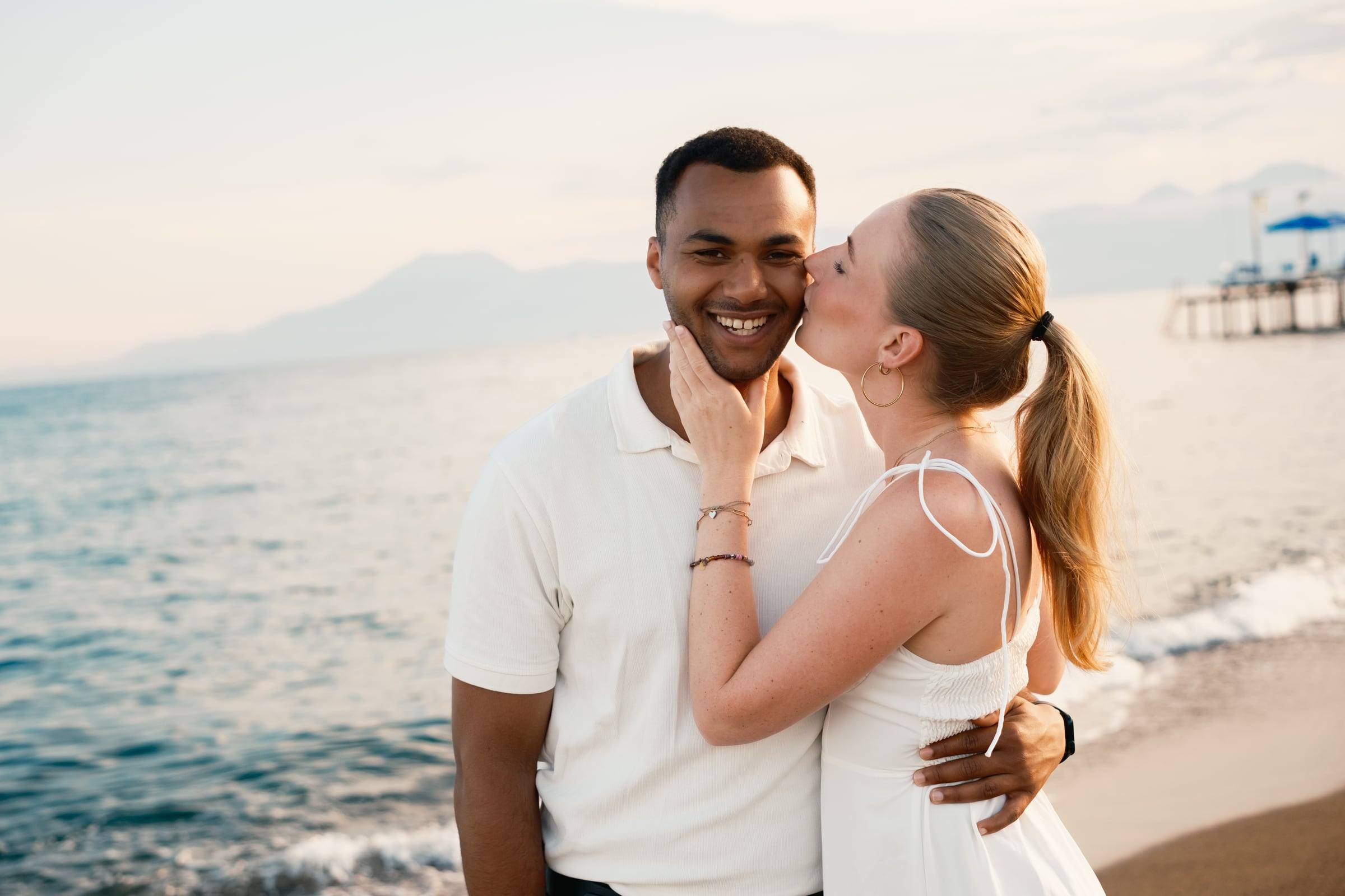 Woman kissing her partner's cheek on the beach at sunset