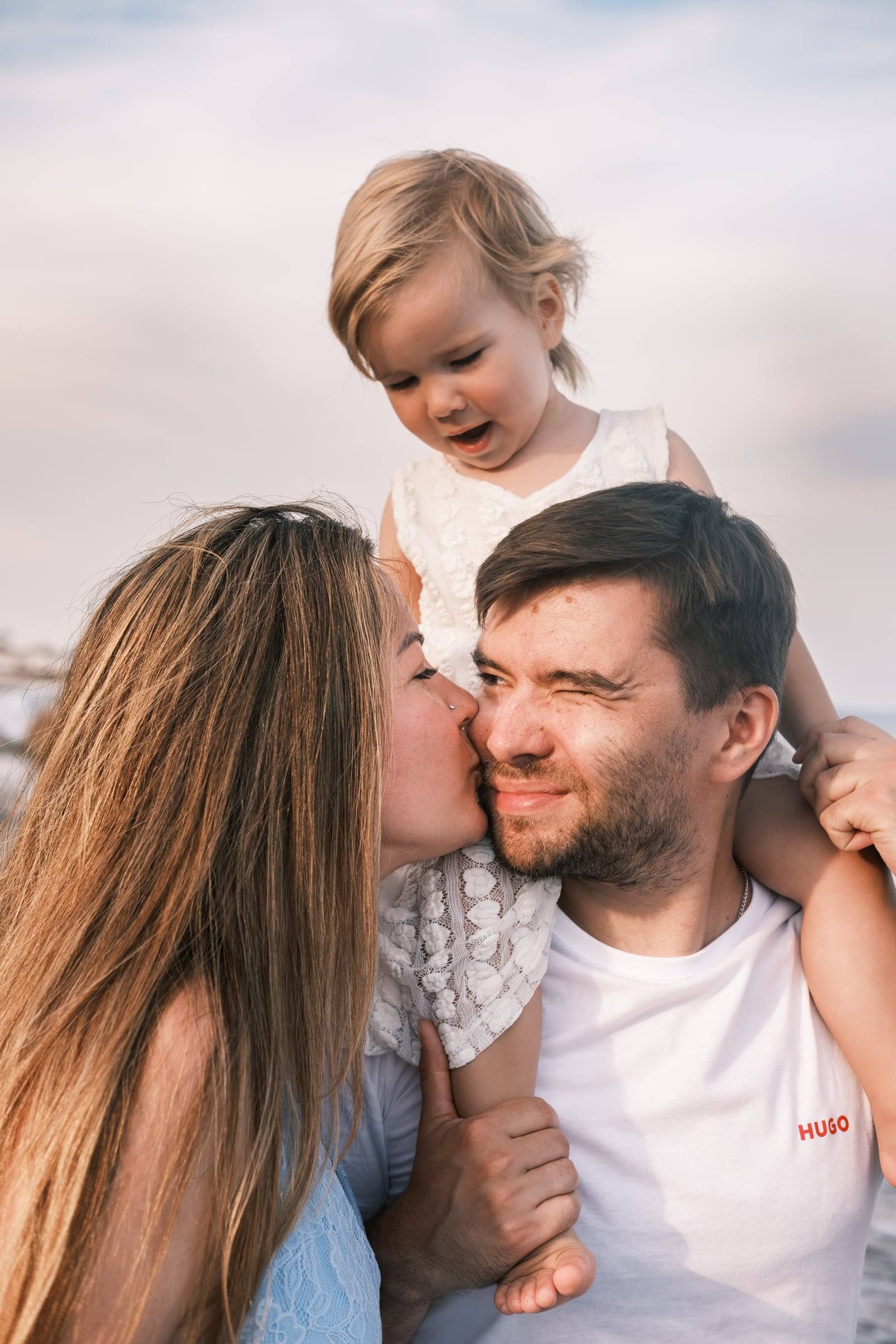 Toddler on dad’s shoulders while mum kisses him