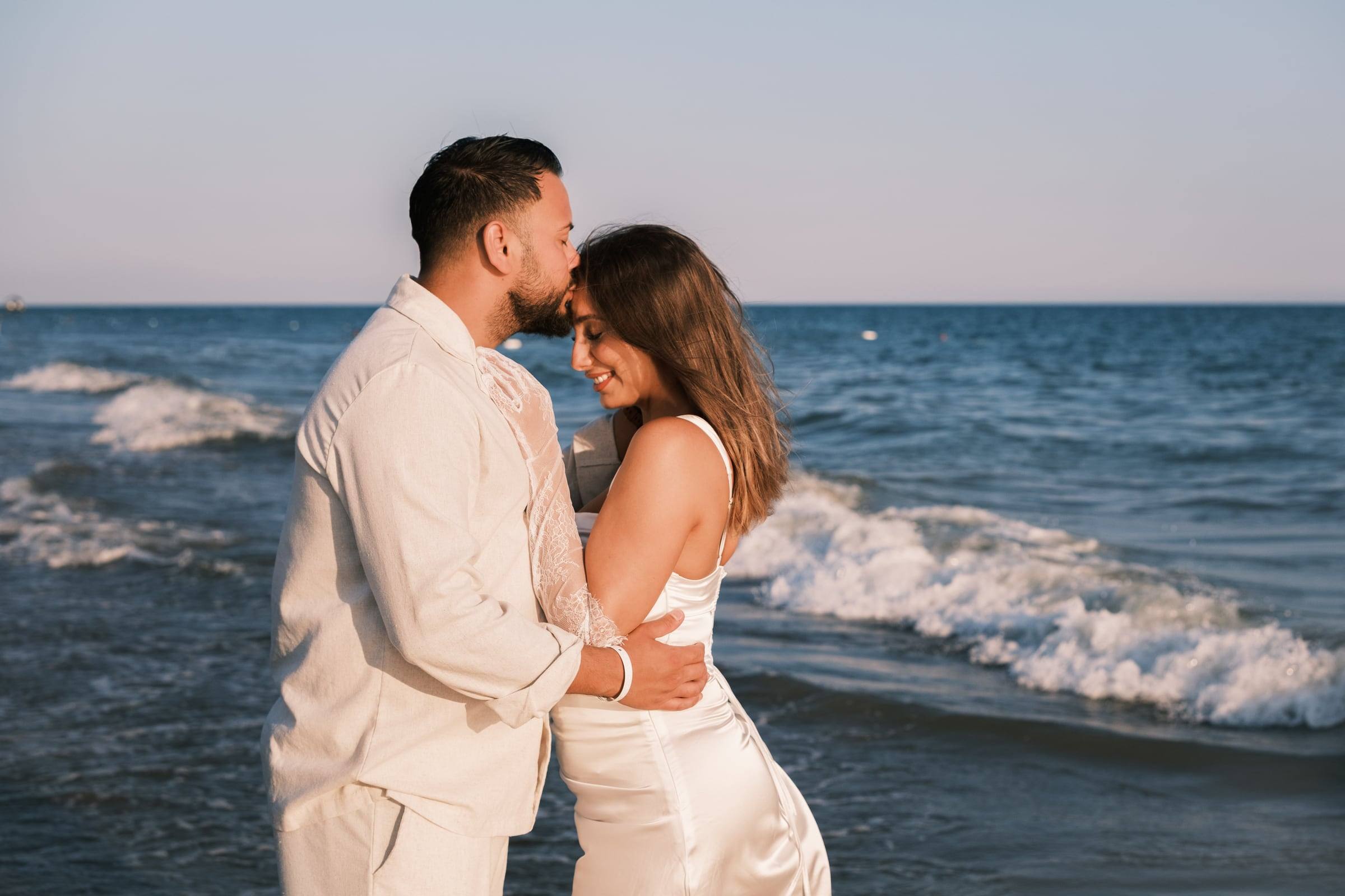 Couple in white touching foreheads by the waves