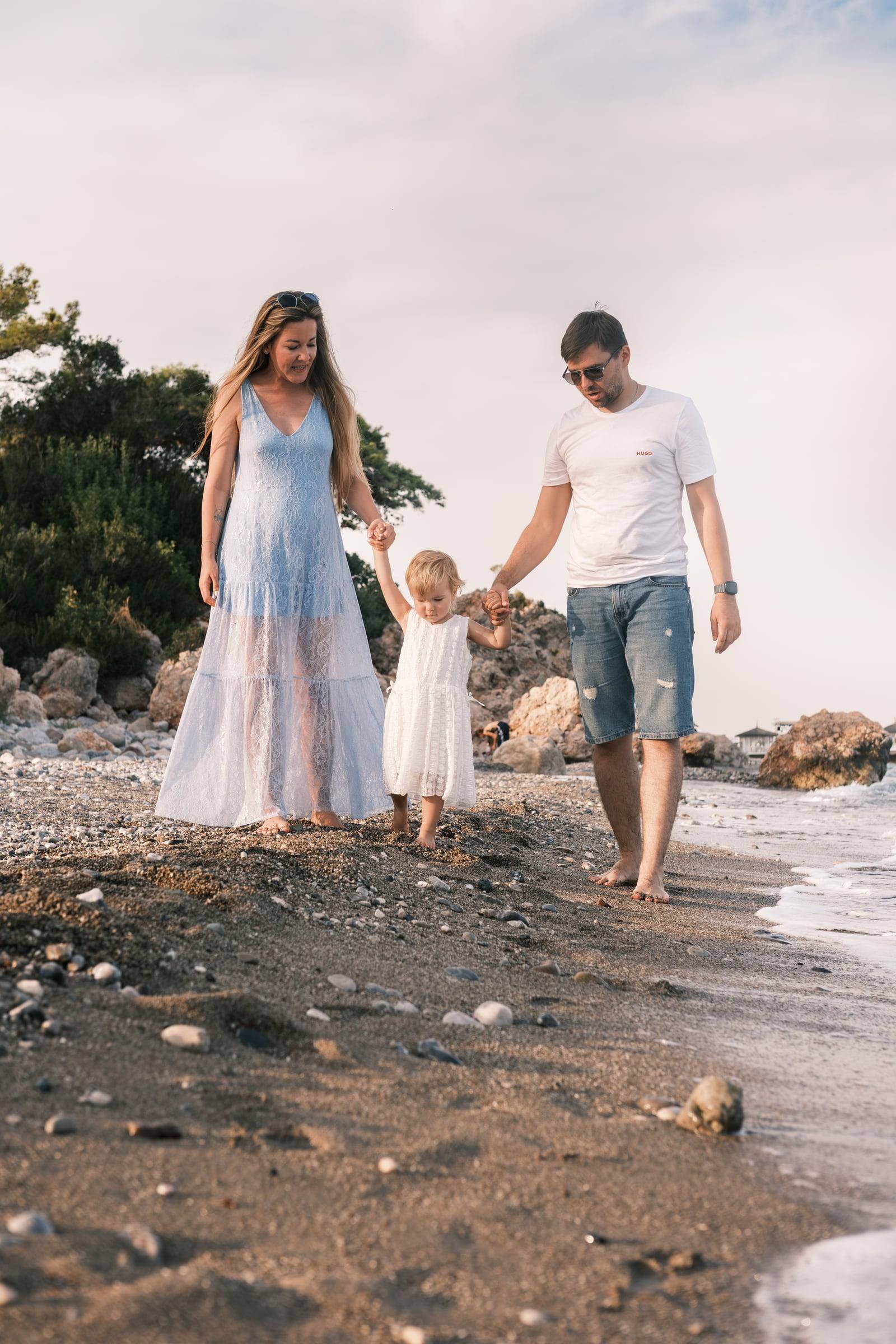 Family walking hand in hand with their toddler along the shore