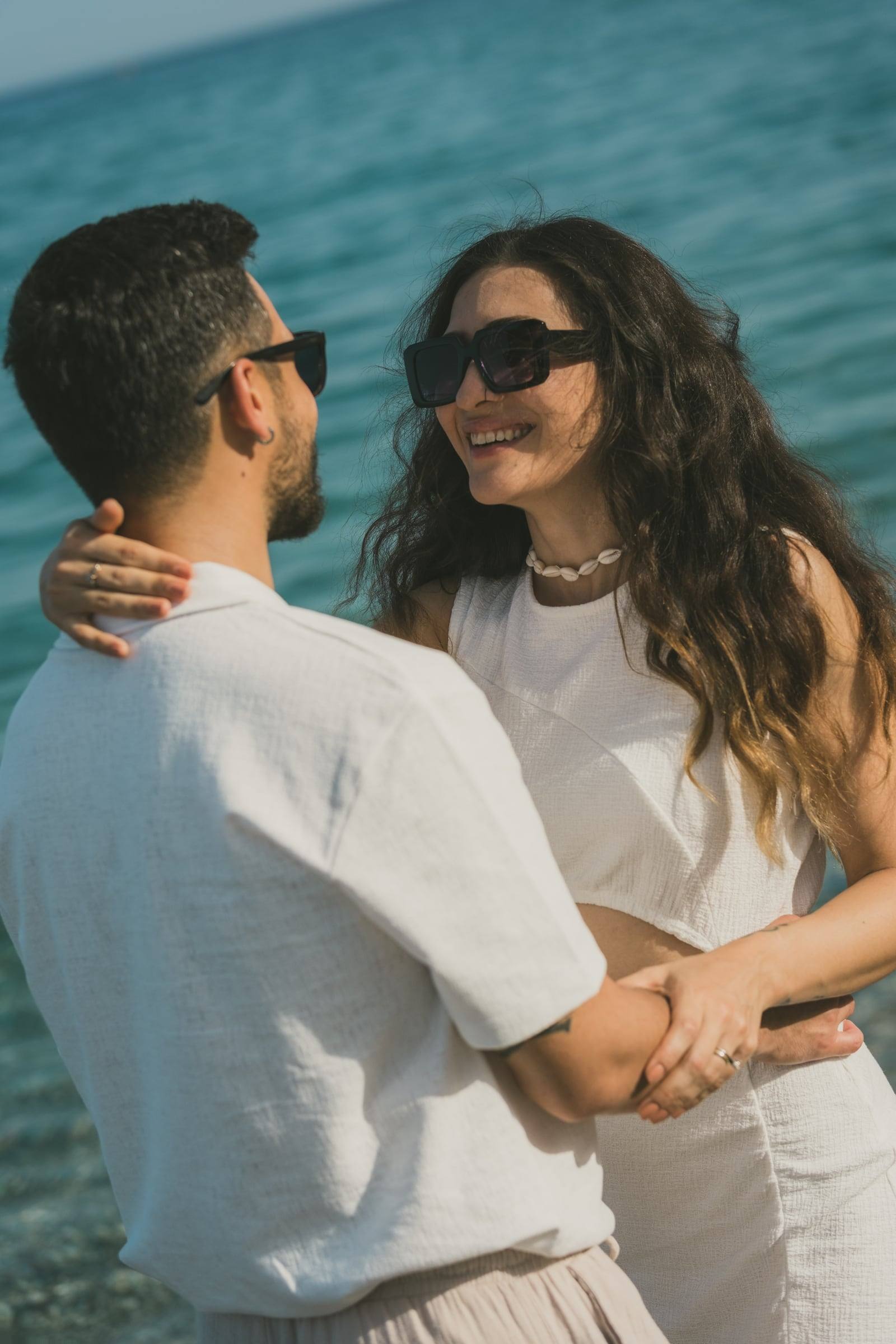 Laughing couple in sunglasses hugging by the sea