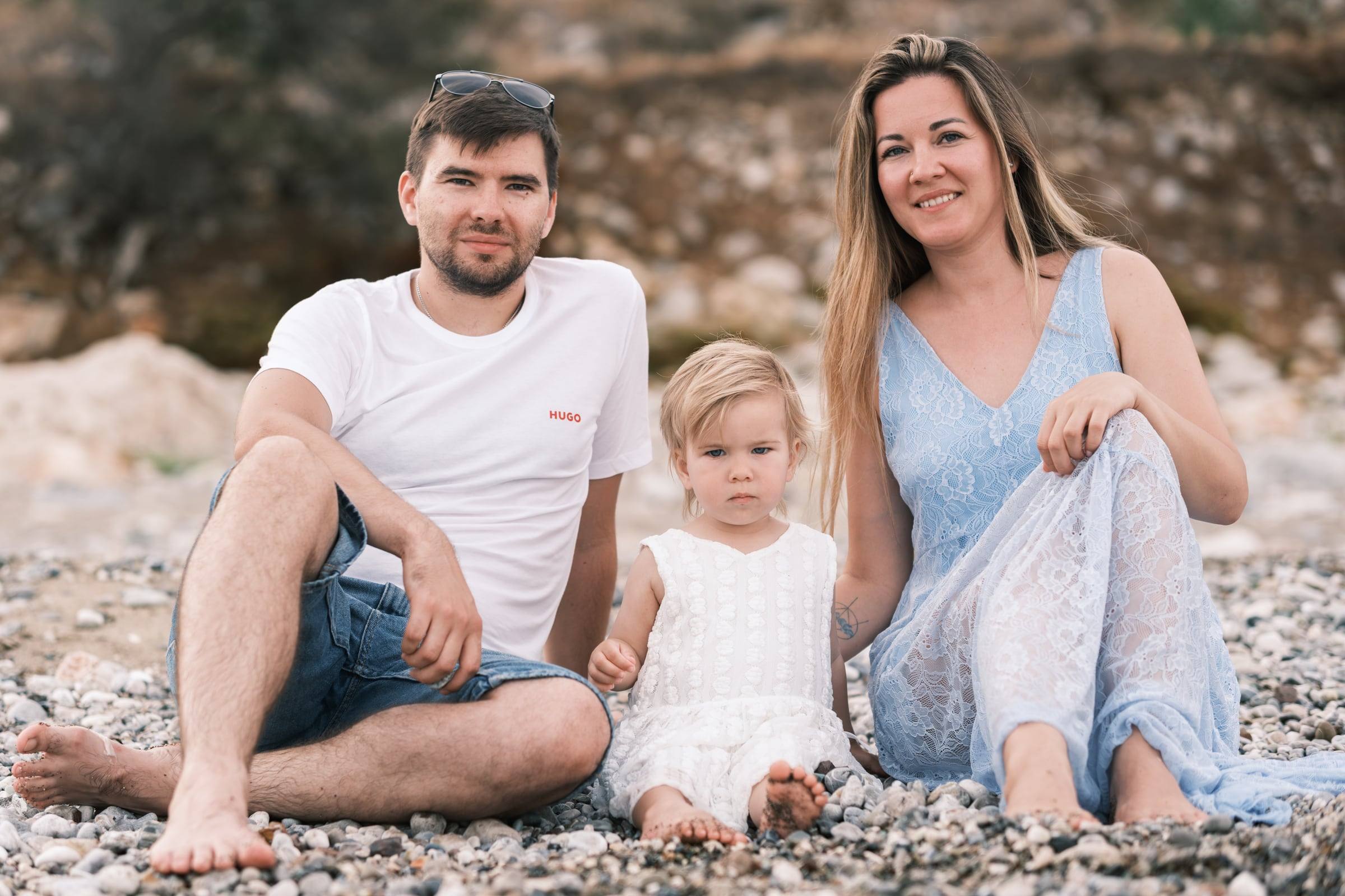 Parents and their little daughter sitting on a pebble beach