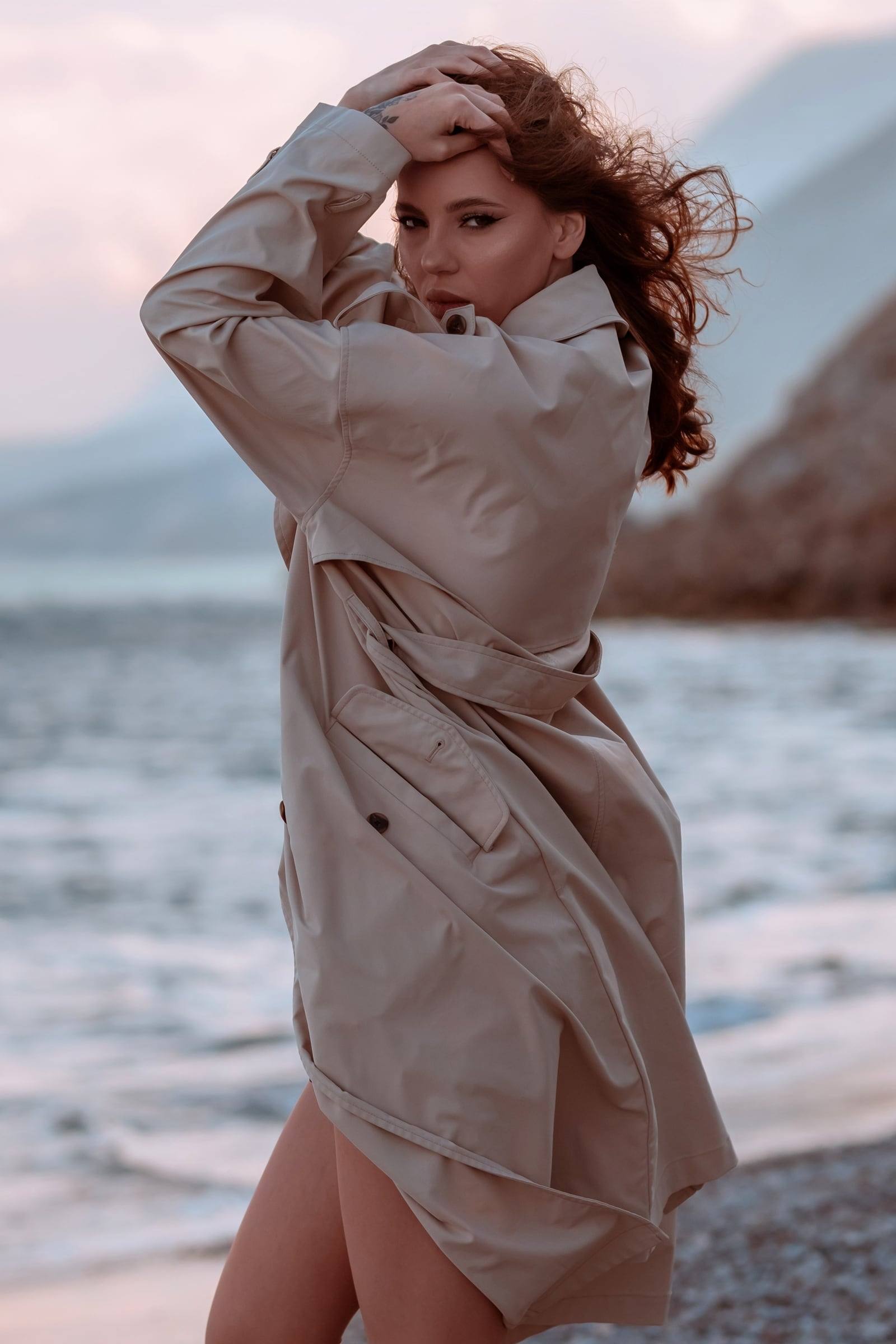 Red-haired woman in a trench coat on a windy beach