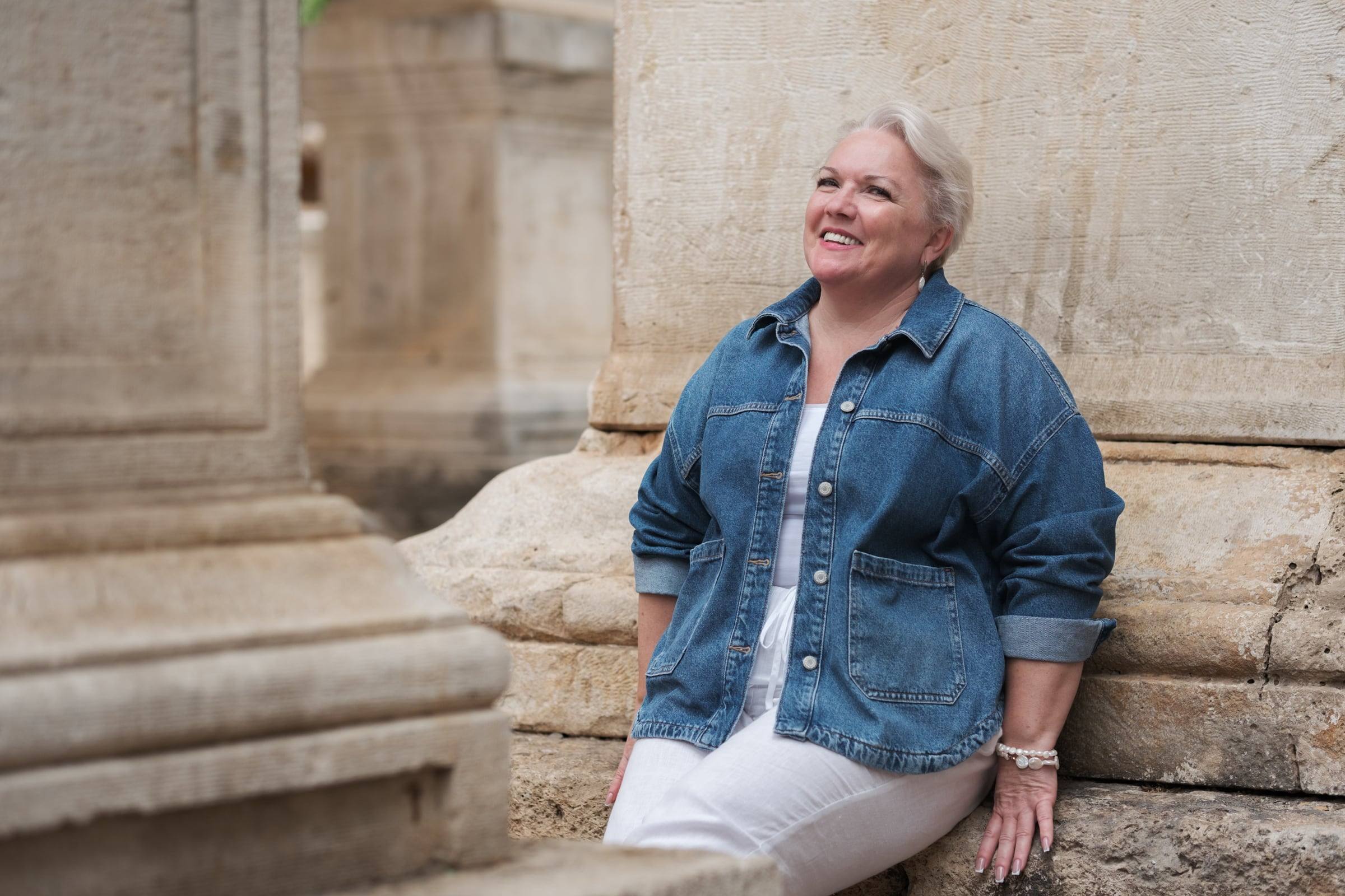 Woman in a denim jacket sitting by ancient marble