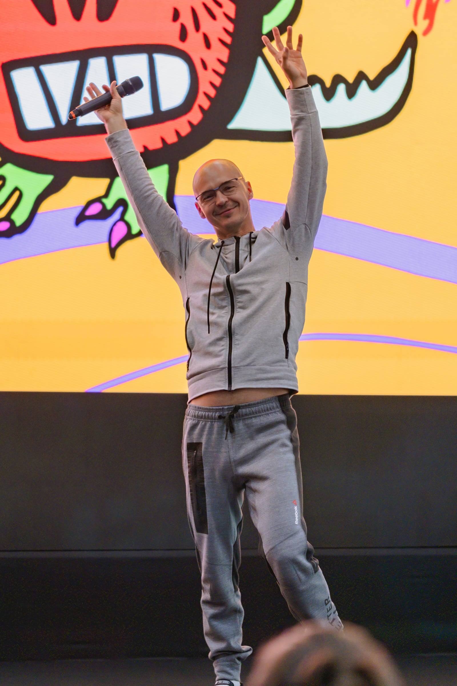 Speaker raising his arms on a colourful stage