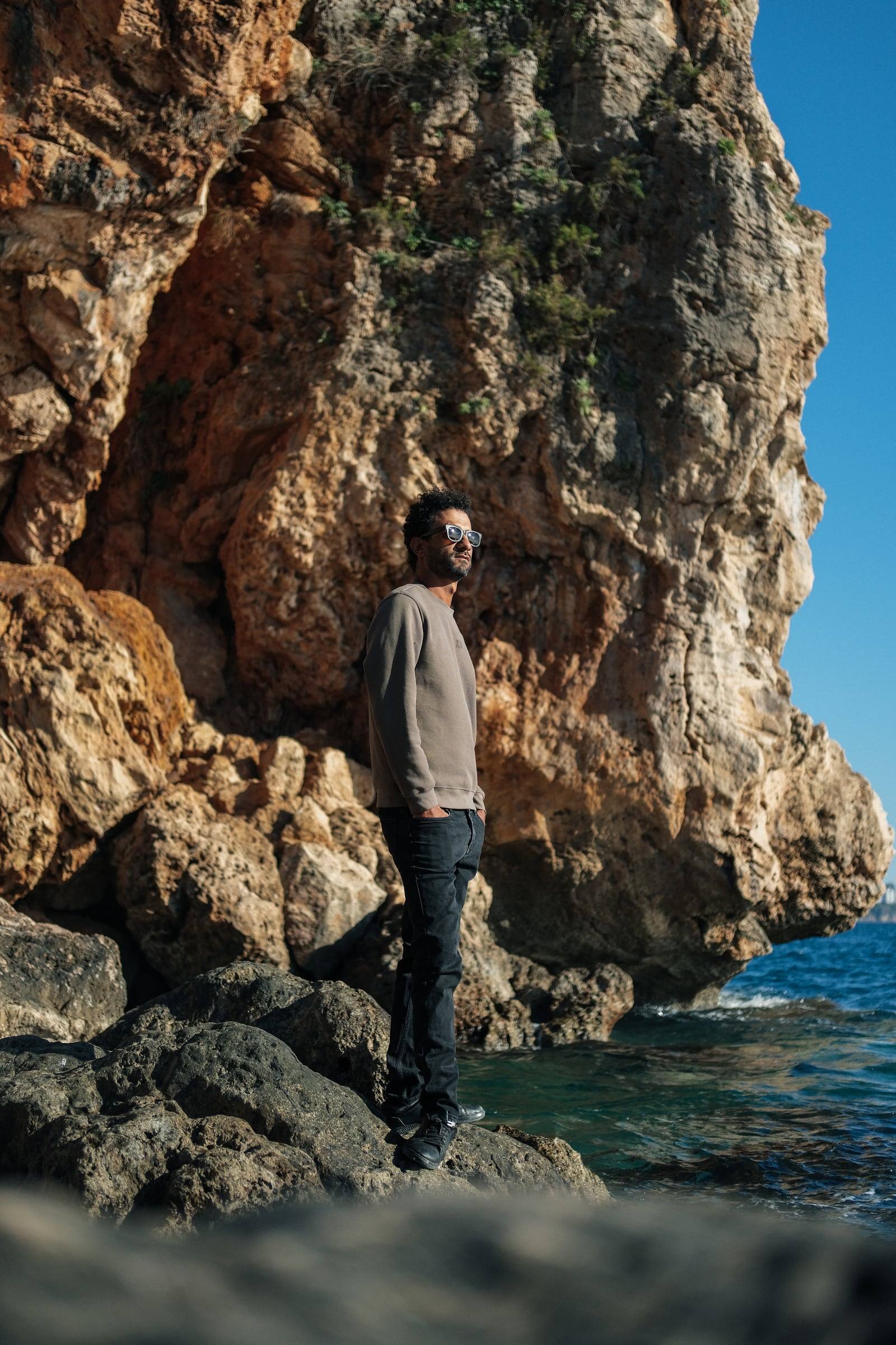 Man standing by a tall rock by the turquoise sea