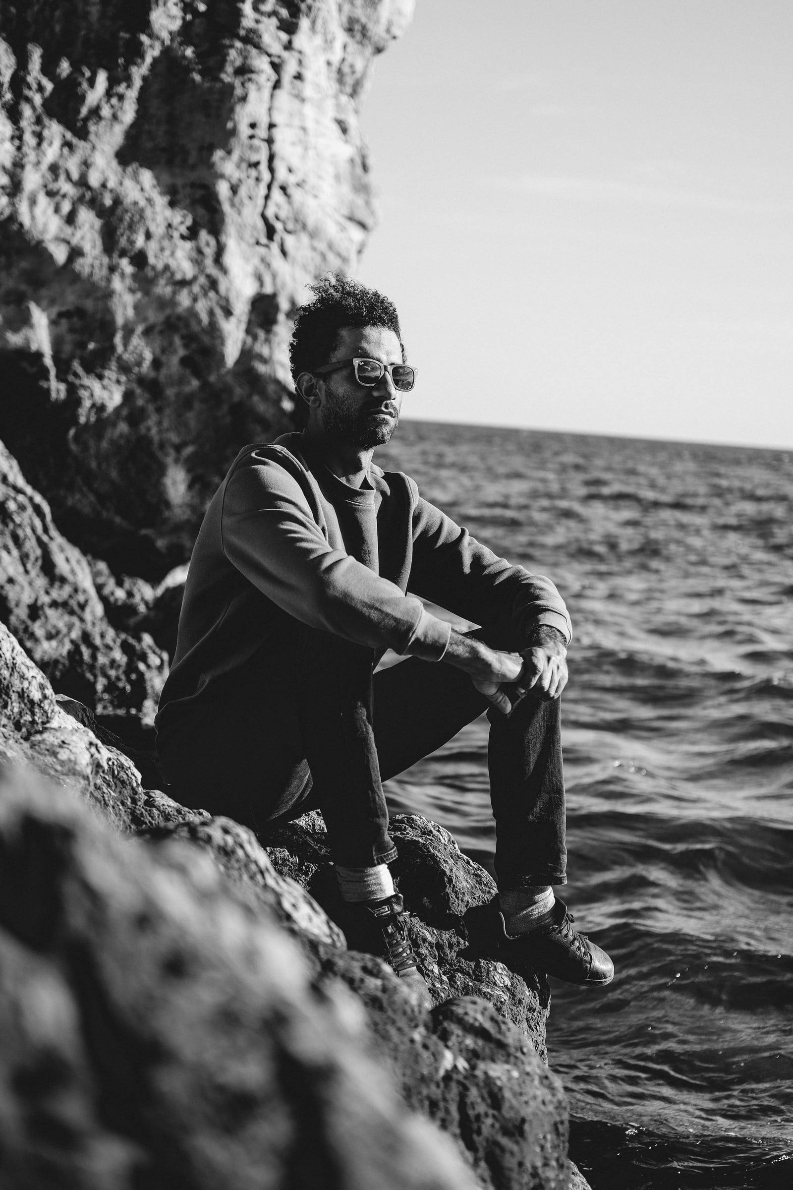 Black-and-white portrait of a man sitting on seaside rocks
