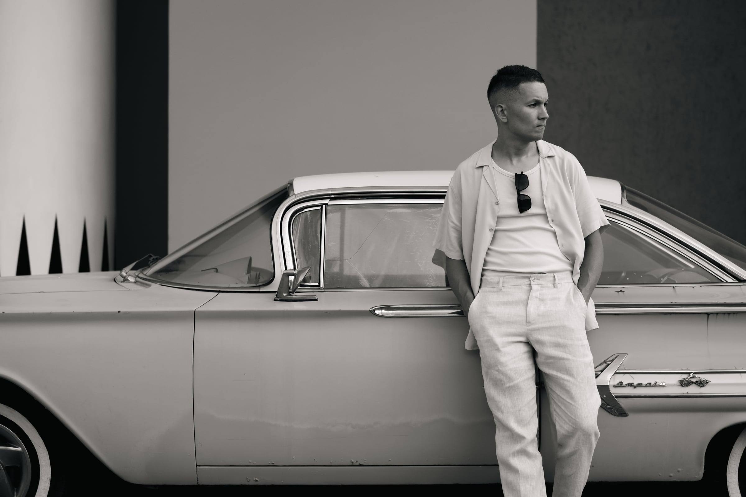 Black-and-white portrait of a man leaning on a vintage car