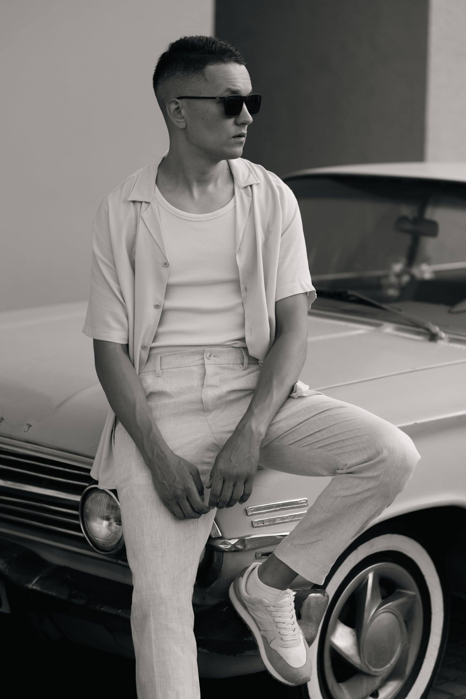 Black-and-white portrait of a man in sunglasses sitting on a vintage car