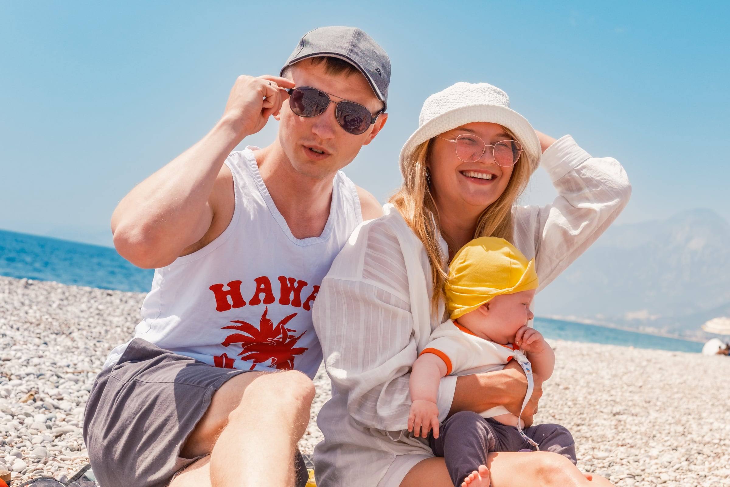 Parents and baby in a yellow hat on a pebble beach