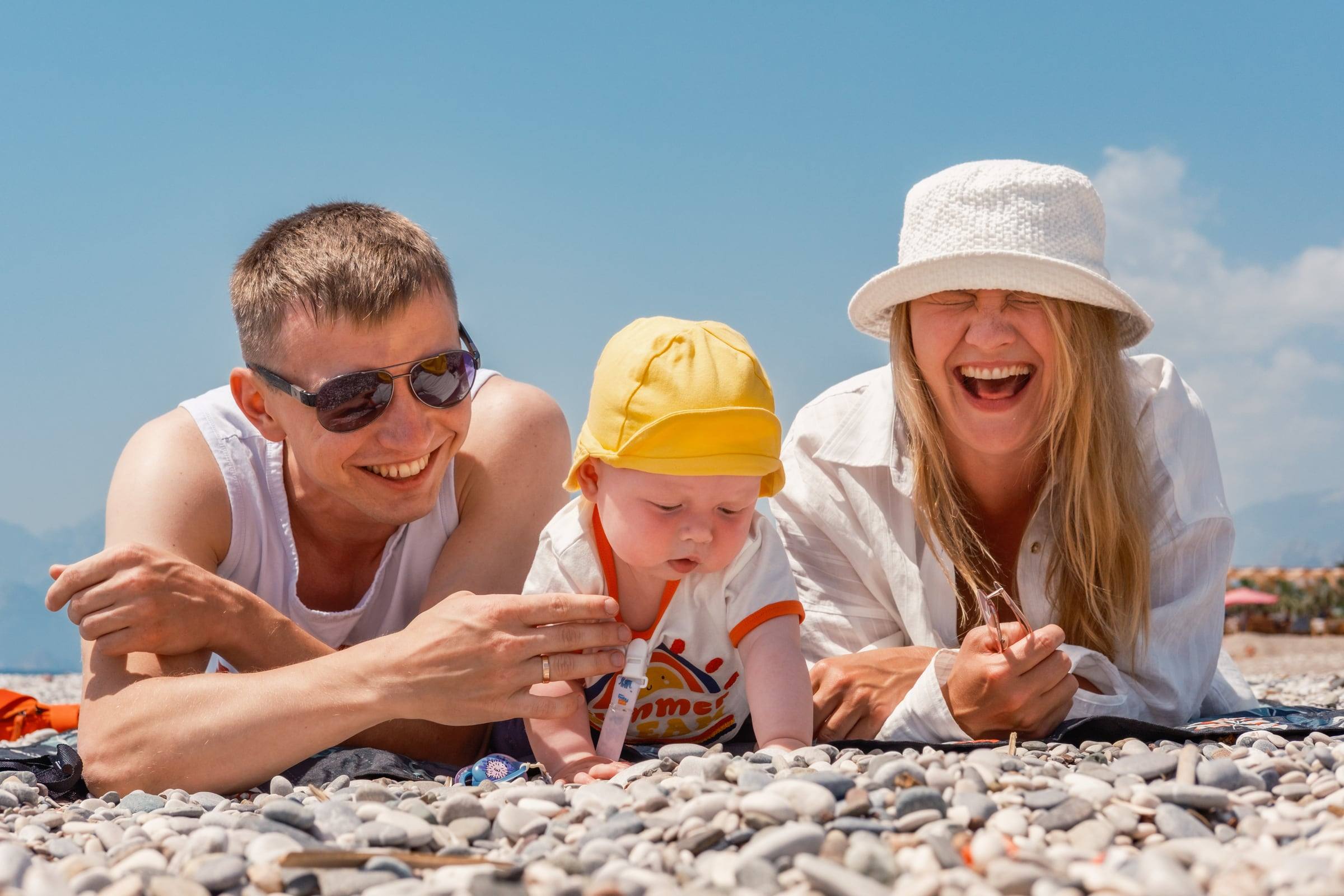 Laughing parents lying on the pebbles with their baby