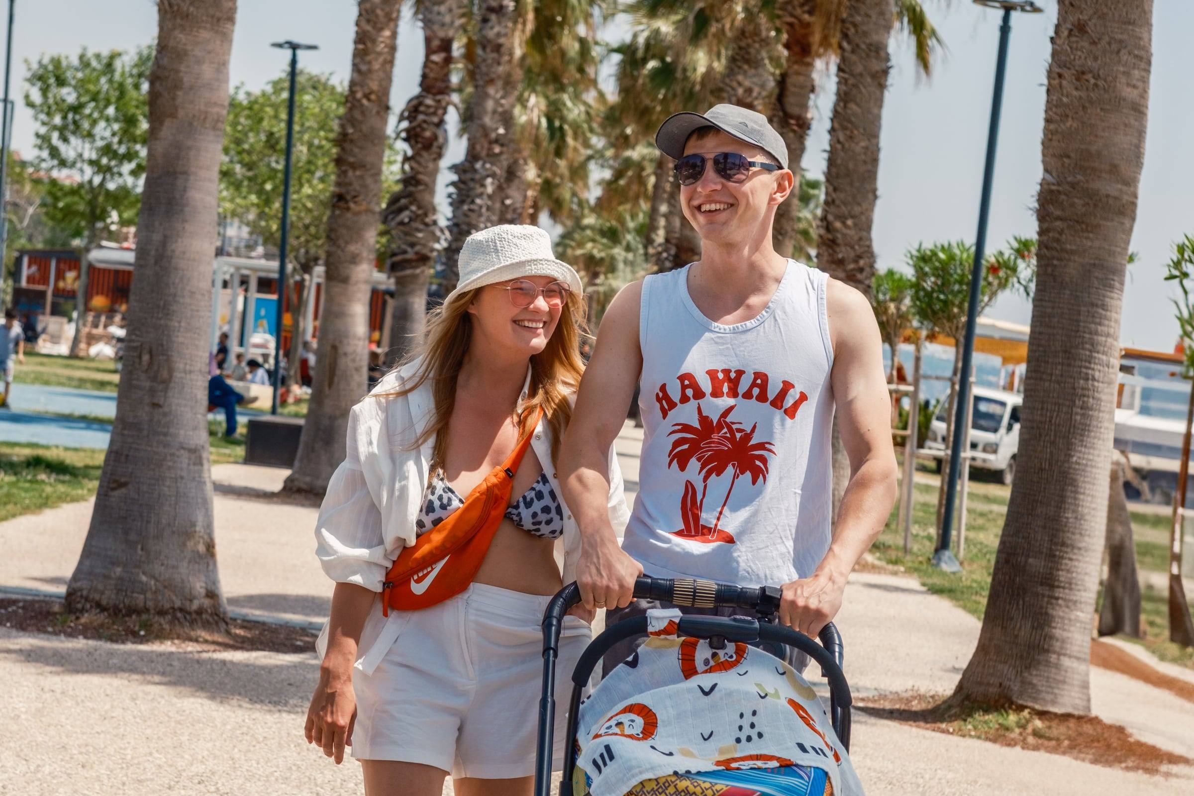 Parents pushing a stroller along a palm-lined seafront