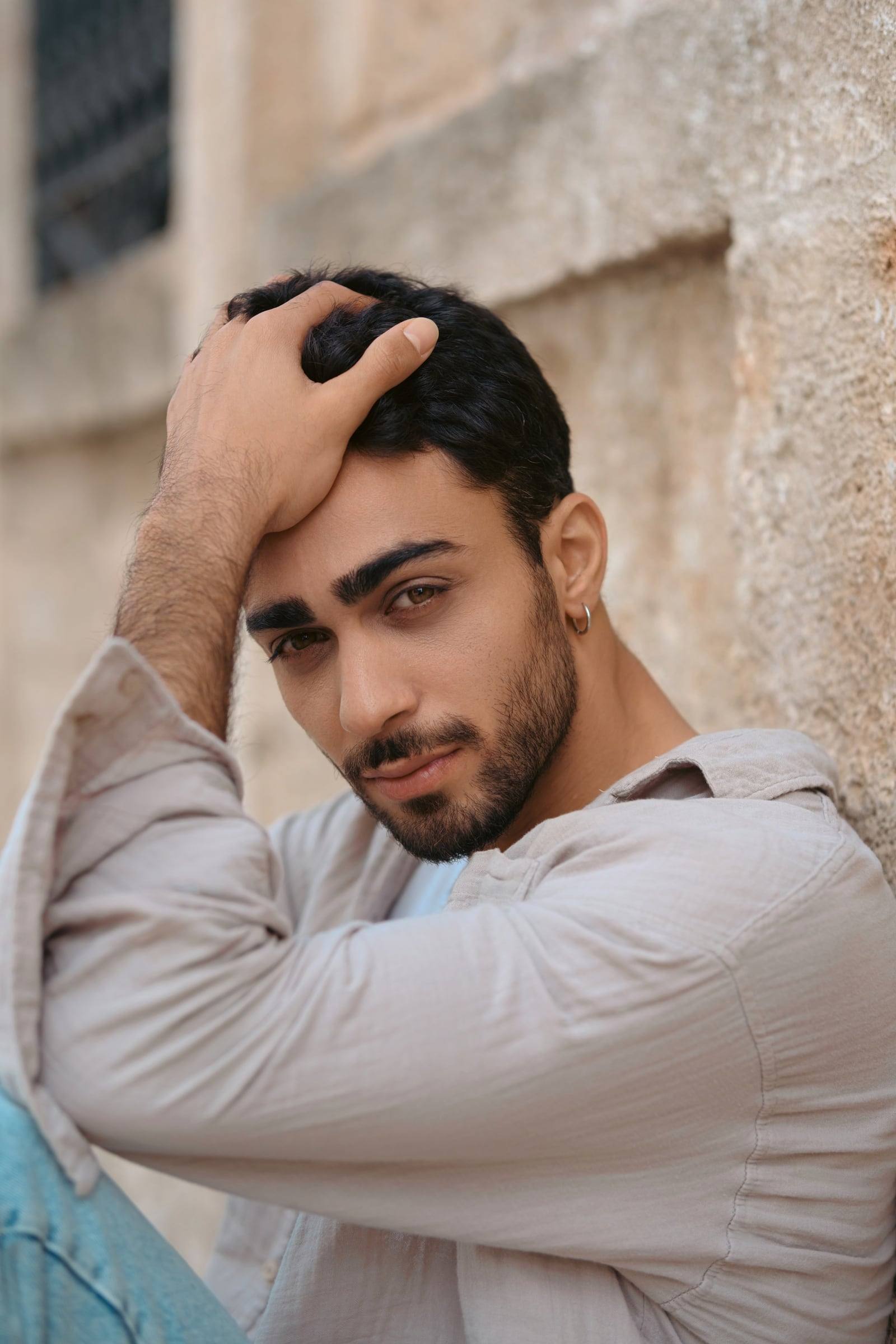 Young man running a hand through his hair by an old wall