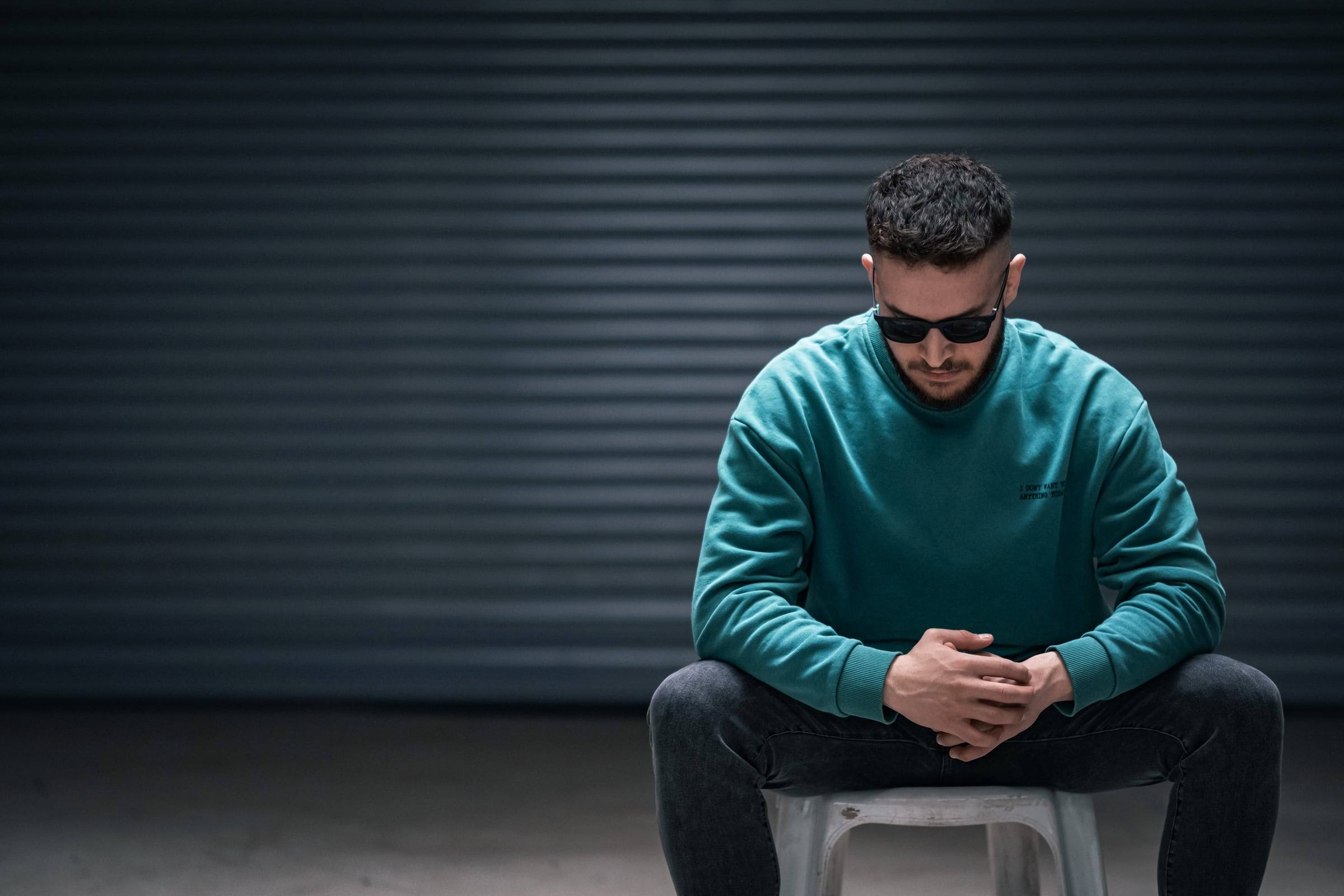 Man in a teal sweater sitting in front of a shutter door
