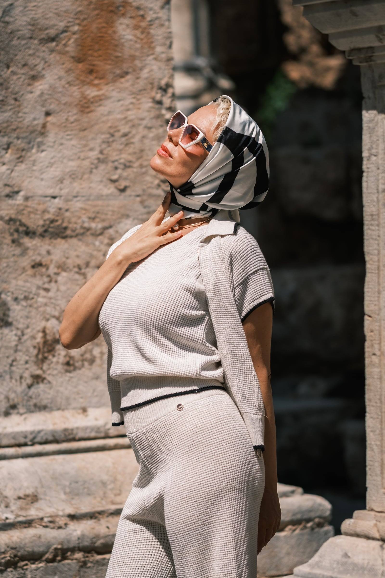 Stylish woman in a silk scarf and sunglasses against ancient stone