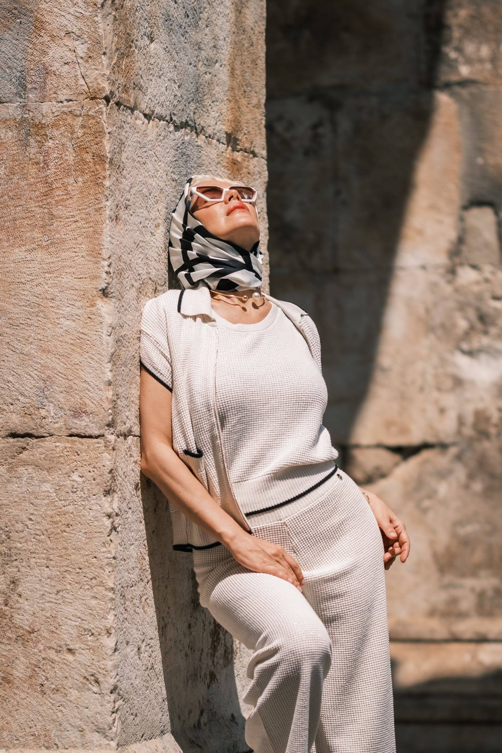 Woman in a cream outfit leaning on a weathered stone wall